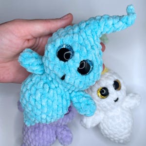May include: Three crocheted ghost plushies with googly eyes. The ghosts are blue, white, and purple.