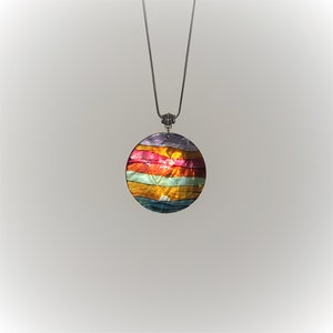 May include: A round, multi-colored iridescent pendant necklace with a silver chain. The pendant has a layered design with shades of purple, pink, orange, yellow, and blue.