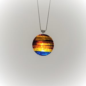 May include: A round shell pendant necklace with a painted sunset scene in shades of red, orange, yellow, and blue. The pendant is attached to a silver chain.