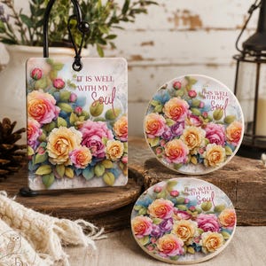 May include: A rectangular hanging ornament and two circular coasters featuring a floral print of pink, yellow, and orange roses with green leaves. Each piece displays the text "IT IS WELL WITH MY SOUL" in a decorative script font.