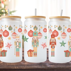 Puede incluir: Tres vasos de vidrio esmerilado con tapas de bambú y pajitas. Cada vaso presenta un diseño navideño con un cascanueces, adornos y estrellas. Los vasos son perfectos para bebidas navideñas.