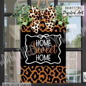 May include: A rectangular door sign featuring a black center panel with the white text HOME and HOME and the orange script text Sweet. The sign has a leopard print border, a large leopard print bow, and green foliage at the top with a rope hanger.