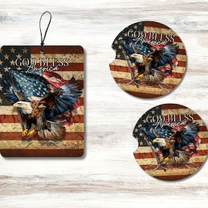 May include: A set of two round coasters and a car air freshener featuring a bald eagle with outstretched wings flying over an American flag. The design includes the text "God Bless America" in a vintage style font.