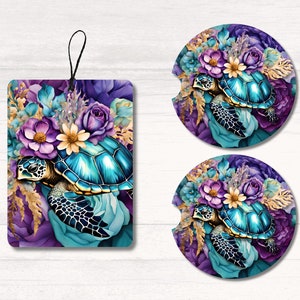 May include: A set of car accessories featuring a teal sea turtle design surrounded by purple, teal, and gold floral elements. The set includes two round car coasters and a rectangular air freshener with a black string for hanging.