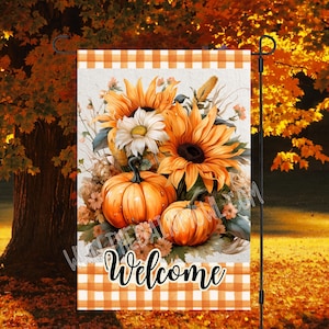 Puede incluir: Una bandera de jardín de bienvenida con un tema otoñal. La bandera presenta un fondo blanco con bordes a cuadros naranja y blancos. El centro de la bandera presenta un ramo de girasoles y calabazas con la palabra "Bienvenido" impresa en negro.