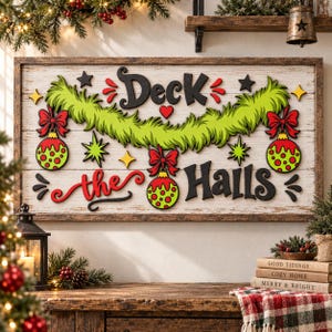 May include: A rectangular wooden wall sign with a white distressed background featuring the black text Deck the Halls. The sign is decorated with a green fuzzy garland, three red and green patterned Christmas ornaments, and small stars.