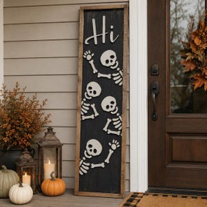 May include: A tall, rectangular wooden sign with a dark black vertical plank background and a natural wood frame. The sign features the white text "Hi" at the top, followed by three white skeleton figures arranged vertically, each with arms raised in a waving gesture.