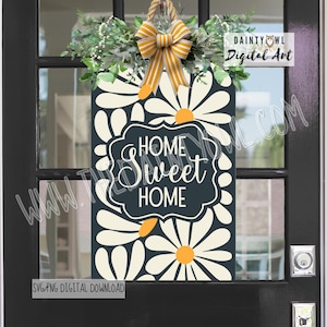 May include: A rectangular wooden sign with a daisy pattern and the words "Home Sweet Home." The sign is decorated with greenery and a yellow and white striped bow. The sign is hanging on a black door.