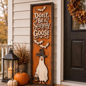 May include: A tall rectangular wooden sign with a dark frame and orange background featuring the text Don't Be a Scaredy Goose, three cutout bats, and a white goose wearing a black witch hat while holding a small orange jack-o'-lantern bucket.