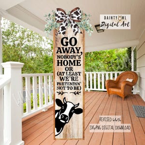 May include: A vertical wooden sign with a light brown wood grain texture, featuring a black and white cow print bow at the top with green foliage. The text reads: GO AWAY, NOBODY'S HOME OR (AT LEAST WE'RE PRETENDIN' NOT TO BE) above a black cow head.