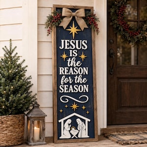Puede incluir: Un letrero de madera rectangular alto con fondo azul oscuro y marco de madera natural. Presenta el texto blanco 'JESUS IS the REASON for the SEASON', estrellas doradas, un lazo de arpillera y una silueta blanca de un pesebre en la parte inferior.