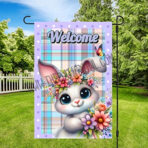 Puede incluir: Una bandera de jardín de cuadros azules y morados con lunares blancos. La bandera presenta un conejito de dibujos animados con una corona de flores y un ramo de flores. El texto "Welcome" está impreso en blanco en la bandera.