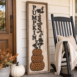 May include: A tall rectangular wooden sign with a light wood grain finish featuring the black vertical text PUMPKIN and the cursive word season. Below the text is a stack of three orange pumpkins with a black leopard print pattern.