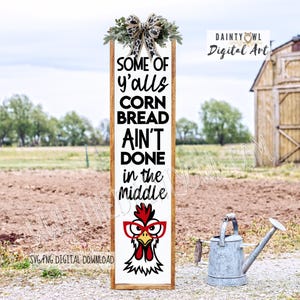 Peut inclure: Panneau rectangulaire en bois avec le texte "SOME OF y'alls CORN BREAD AIN'T DONE in the Middle". Le panneau présente un dessin de poulet portant des lunettes. Le haut est décoré de verdure et d'un nœud. Un arrosoir est à l'arrière-plan.