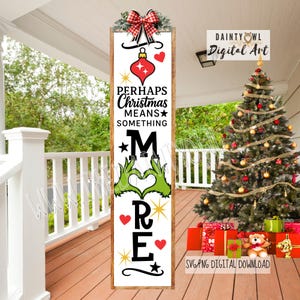 Puede incluir: Un letrero vertical de madera con el texto "Perhaps Christmas Means Something More". El letrero presenta una bola roja, corazones, estrellas y manos verdes formando un corazón. Un lazo a cuadros rojo y blanco adorna la parte superior. Decoración navideña.