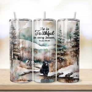 May include: A stainless steel tumbler with a watercolor design of a snowy forest scene with a black bear. The tumbler has a straw and the text "He is Faithful in every Season, Psalm 119:90".