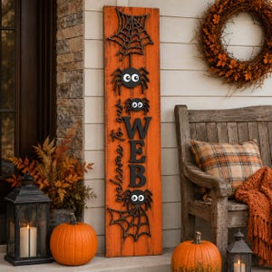 May include: A tall, rectangular orange wooden sign featuring black spider web cutouts at the top and bottom, three black spiders with large white eyes, and the black text "Welcome to our WEB" vertically oriented in the centre of the board.