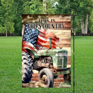 May include: A green tractor with an American flag in the background. The flag is painted in a watercolor style. The text "This is God's Country" is printed on the flag.