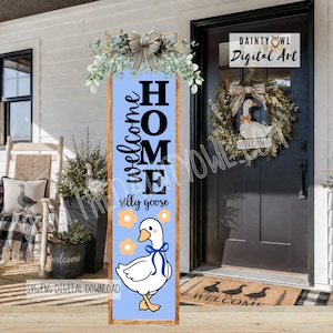 May include: A wooden welcome sign with a light blue background and the words "Welcome Home" in black script and block letters. A cartoon goose with a blue bow is at the bottom. The sign is decorated with greenery and a bow at the top.