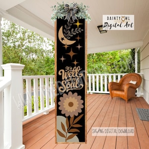 Puede incluir: Un letrero vertical de madera con fondo negro presenta una luna creciente, estrellas y un diseño floral. El texto "It is well with my Soul" se muestra en una fuente decorativa. El letrero está adornado con vegetación y un lazo a rayas en la parte superior.