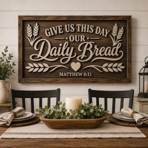 Op de afbeelding: Een rechthoekig houten wandbord met een donkerbruine afwerking voorzien van verhoogde lichtgekleurde tekst GIVE US THIS DAY OUR Daily Bread en MATTHEW 6:11, geaccentueerd met tarwe-illustraties en een klein hartje onder de tekst.