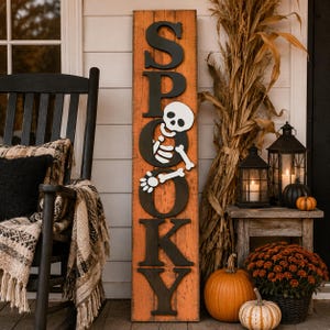 Könnte beinhalten: Ein hohes, rechteckiges orangefarbenes Holzschild mit schwarzer vertikaler Beschriftung, die das Wort SPOOKY bildet. Eine weiße Skelettfigur ist über dem Buchstaben O angebracht, wobei Arme und Beine über die Oberfläche des Schildes ragen.