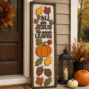 May include: A tall rectangular wooden sign with a white distressed background and dark brown frame. The sign features the text "FALL for JESUS He never LEAVES" in dark brown lettering, decorated with orange, yellow, red, and green wooden leaves and acorns.
