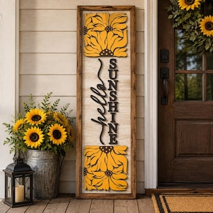 May include: A tall rectangular wooden sign with a light-coloured background, featuring a dark brown frame, yellow sunflower cutouts at the top and bottom, and the black text "hello SUNSHINE" written vertically in the centre of the sign.