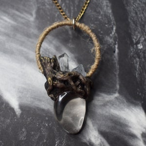 Puede incluir: Un collar con un colgante de cristal de cuarzo transparente, envuelto en alambre marrón y dorado. El colgante está suspendido de una cadena dorada.