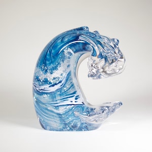 Pode incluir: Escultura decorativa em vidro em forma de onda. A onda &eacute; uma mistura de azul e branco, com um padr&atilde;o em espiral. A crista da onda &eacute; de vidro transparente. Em um fundo branco.