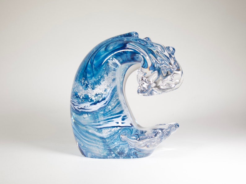 Pode incluir: Escultura decorativa em vidro em forma de onda. A onda &eacute; uma mistura de azul e branco, com um padr&atilde;o em espiral. A crista da onda &eacute; de vidro transparente. Em um fundo branco.