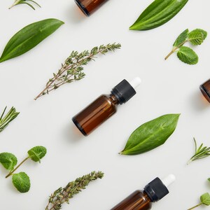 May include: A flat lay of essential oil bottles with droppers and various green herbs on a white background. The herbs include rosemary, thyme, and mint.