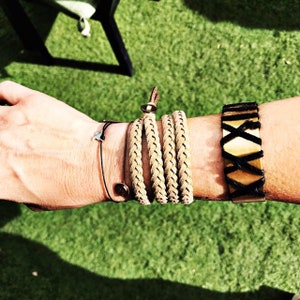 May include: A collection of bracelets in various styles. There is a black string bracelet with a star charm, a braided tan leather wrap bracelet, and a wide tan leather bracelet with black crisscross stitching.