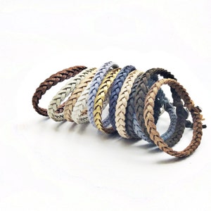 May include: A collection of braided leather bracelets in various colors, including brown, beige, blue, and gray. The bracelets are arranged in a curved line, showcasing their different hues and textures. Each bracelet appears to be approximately 0.5 inches wide.