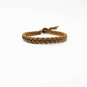 May include: A braided brown leather bracelet with a loop and toggle closure. The bracelet is made of interwoven strips of leather, creating a textured, woven appearance. The bracelet is shown against a white background.