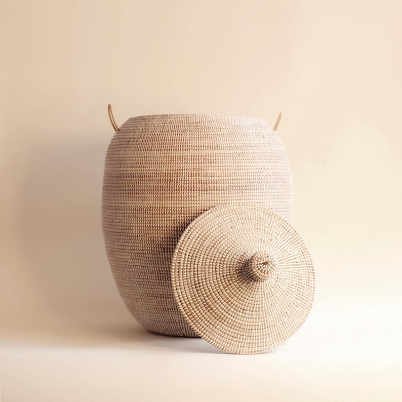 May include: A large, round, woven basket with a lid. The basket is made of natural materials and has a light brown colour. The lid is also woven and has a small knob on top.