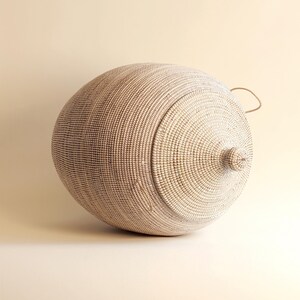 May include: A large, white, round woven basket with a lid and a handle. The basket is made of natural materials and has a natural, rustic look.