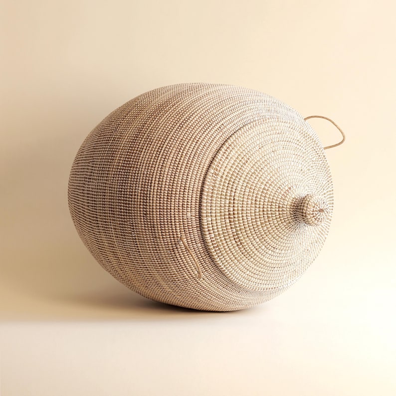 May include: A large, white, round woven basket with a lid and a handle. The basket is made of natural materials and has a natural, rustic look.