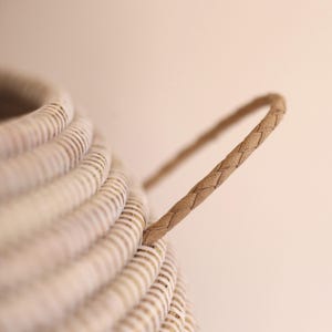 May include: A white wicker basket with a woven leather handle. The basket is made from natural materials and has a rustic look.