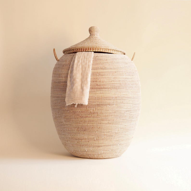 May include: A large, white woven basket with a lid and handles. The basket is made of natural materials and has a natural, earthy look. It is a great storage solution for any home.