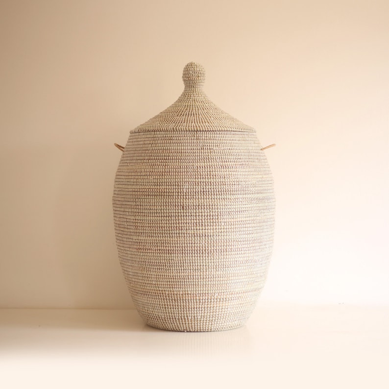 May include: A large, white woven storage basket with a lid and two handles. The basket is made of natural materials and has a traditional design.
