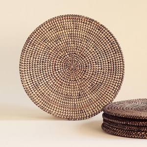 Peut inclure: Ensemble de sets de table ronds en osier de couleur brun naturel et noir. Les sets de table sont faits d'un matériau tissé, peut-être du rotin ou du bambou.