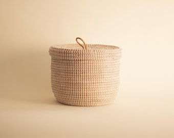 May include: A white woven basket with a lid and a leather handle. The basket is round and has a natural woven texture.