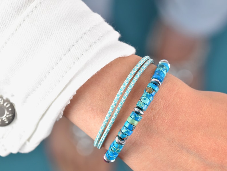 May include: A set of two bracelets consisting of one thin, light blue cord bracelet with a textured surface and one beaded bracelet featuring cylindrical turquoise stone beads with blue and green marbling, interspersed with small silver-toned spacers.