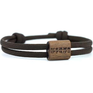 Könnte beinhalten: Ein braunes Paracord-Armband mit einem Holzperlen-Anhänger mit den Koordinaten "51° 8' 28.38" N 17° 2' 18.73" O".