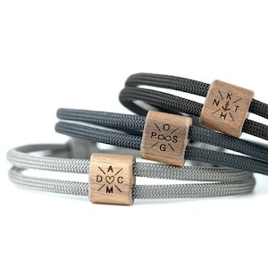 Könnte beinhalten: Drei geflochtene Armbänder aus Seil mit Holzperlen. Die Perlen haben verschiedene gravierte Designs, darunter ein Herz, einen Anker und ein Unendlichkeitszeichen.