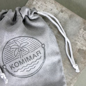 May include: A gray drawstring pouch with a white drawstring. The pouch has a black and white logo with a palm tree and the word "KOMMAR" printed on it.