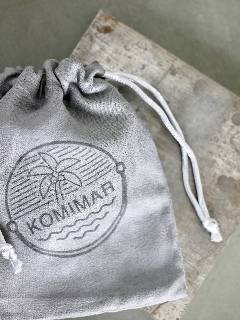 May include: A gray drawstring pouch with a white drawstring. The pouch has a black and white logo with a palm tree and the word "KOMMAR" printed on it.