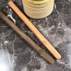 May include: Two wooden stirring sticks, one light brown and one dark brown, on a gray marble surface.