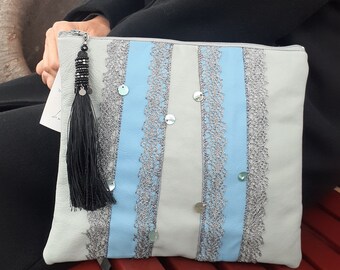 May include: A light gray clutch purse with a blue and silver striped design. The purse has a black tassel and silver sequins.